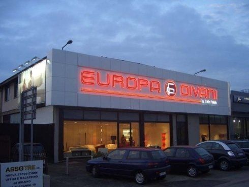 Negozio di mobili Europa Divani con un'insegna illuminata al tramonto, auto parcheggiate fuori.