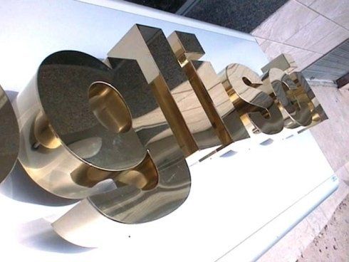 Lettering 3D dorato e lucido di un logo su sfondo bianco. Riflette l'ambiente circostante.