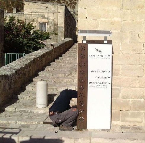 Uomo che lavora su un cartello alto per il San Angelo Resort su una scalinata in pietra all'aperto.