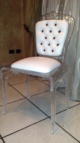 Sedia in acrilico trasparente con seduta bianca e schienale capitonné; dettagli con bottoni scuri.