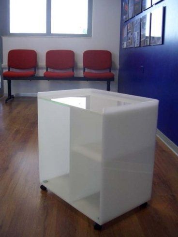 Carrello bianco con ruote in una sala d'attesa con sedie rosse e parete blu.