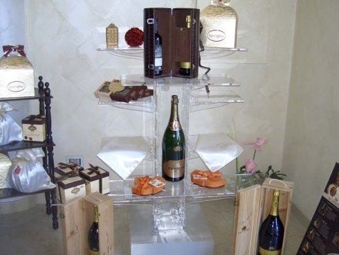 Esposizione di bottiglie di champagne e scatole regalo su ripiani in acrilico trasparente.