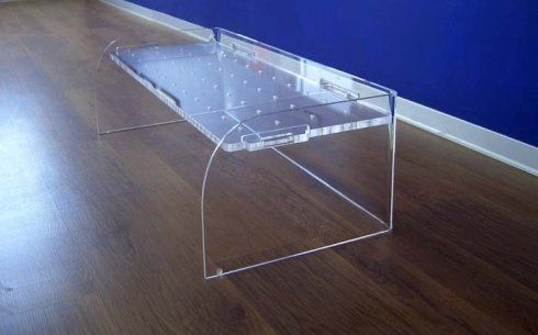 Panca in acrilico trasparente con gambe angolate su un pavimento in legno, contro una parete blu.