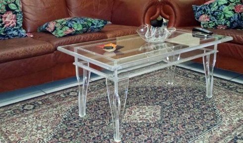 Tavolino da caffè in acrilico con oggetti sopra, di fronte a un divano in pelle marrone su un tappeto a fantasia.