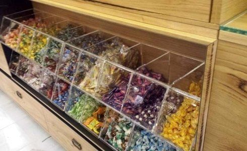 Espositore di caramelle con contenitori trasparenti pieni di caramelle colorate in un mobiletto di legno.