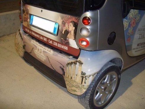 Parte posteriore di una Smart sporca con pubblicità, targa e ruota.