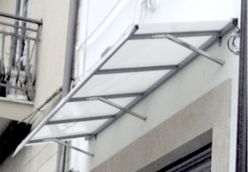 Tenda da sole in metallo grigio con pannelli trasparenti montata sopra una porta.