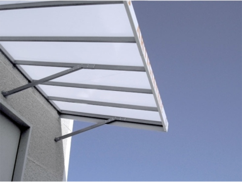 Tenda da sole in metallo grigio con tetto traslucido sopra una porta, fissata a un edificio di colore chiaro contro un cielo azzurro.