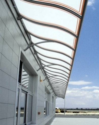 Una tenda da sole ondulata, bianca e marrone, sopra un edificio con finestre che si staglia contro un cielo blu.