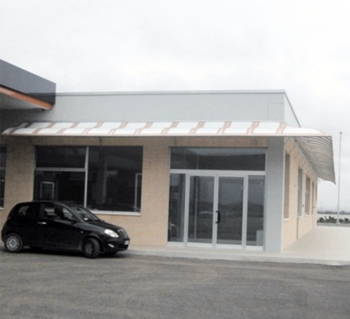 Un'auto nera parcheggiata fuori da un edificio color marrone chiaro con porte e finestre in vetro, sotto una tenda di metallo.