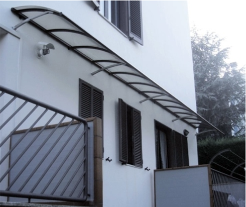 Una tenda curva e trasparente copre le finestre di un edificio bianco. Sono visibili una ringhiera e delle persiane metalliche.