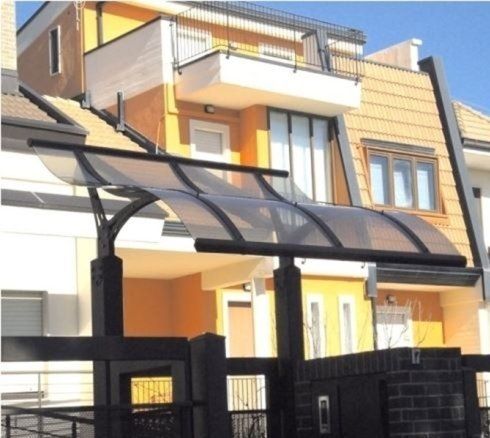 Una tettoia nera sopra la porta di un edificio con pareti gialle e arancioni e una recinzione grigio scuro.