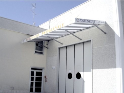 Edificio bianco con una tettoia metallica sopra la porta con la scritta 