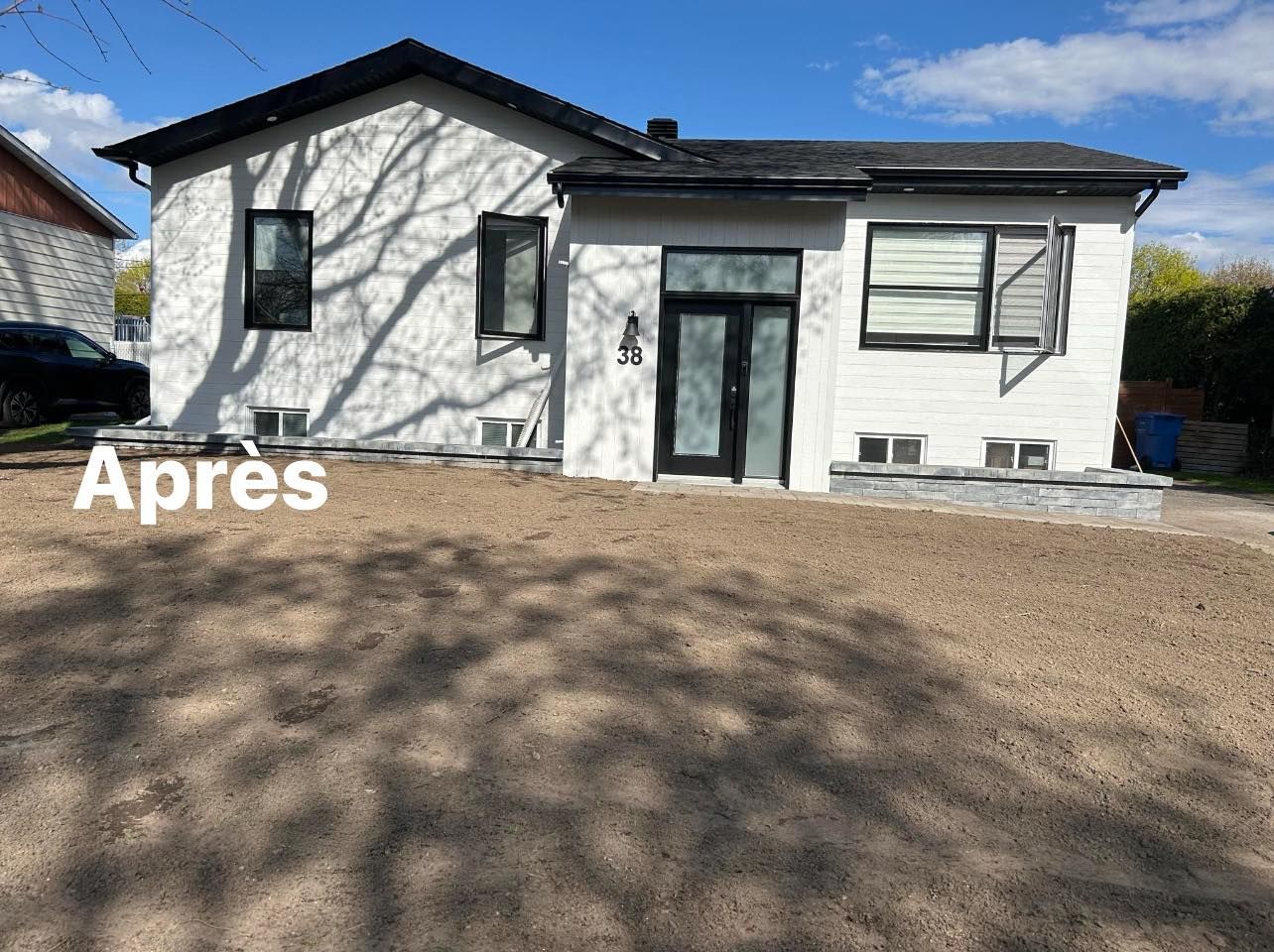 Une maison blanche avec un toit noir et une voiture noire garée devant.