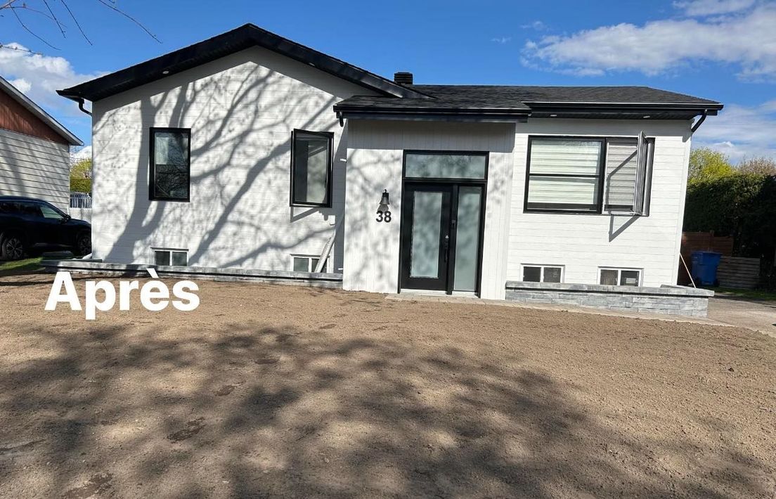 Une maison blanche avec un toit noir et une voiture noire garée devant.