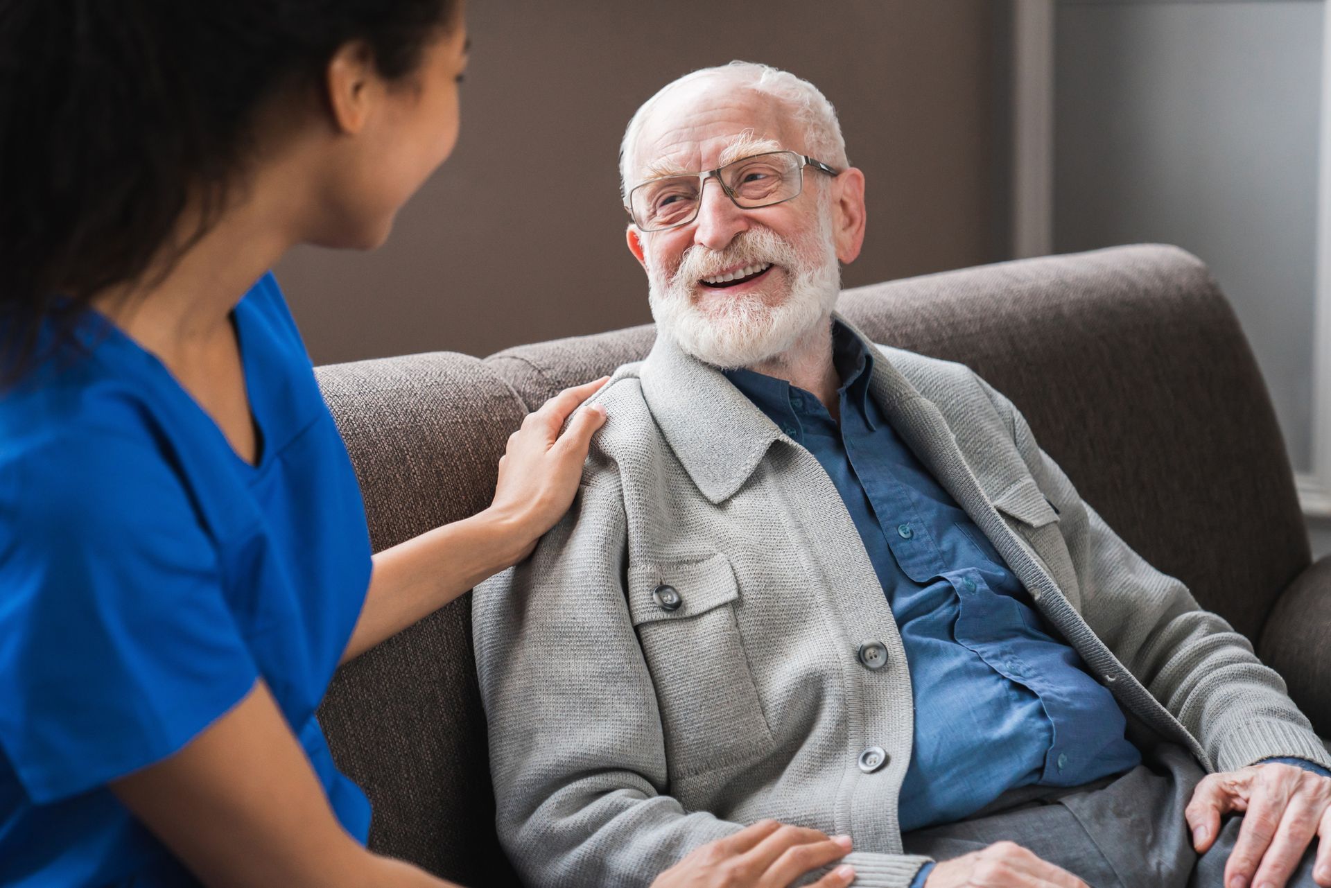 An elderly man is sitting on a couch with a nurse