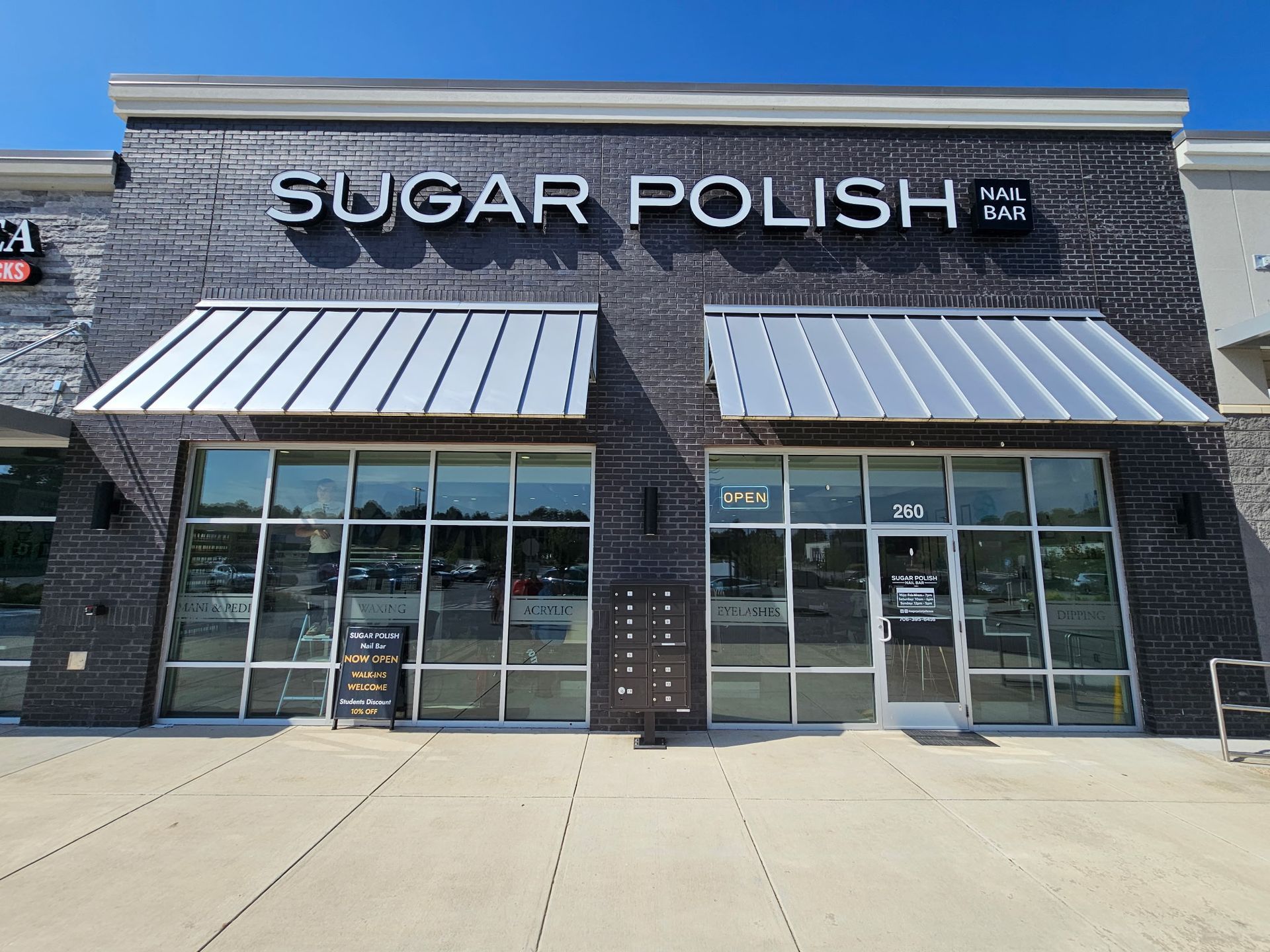Sugar Polish storefront with silver awnings and brick facade on a sunny day.