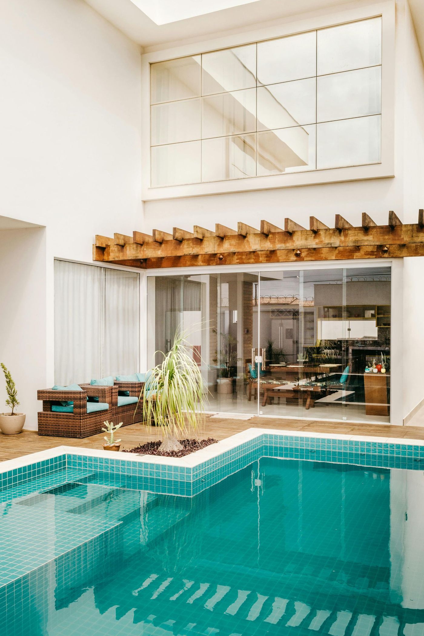 A tranquil indoor pool area with turquoise water, wooden accents, and floor-to-ceiling glass doors leading to a sunlit interior.