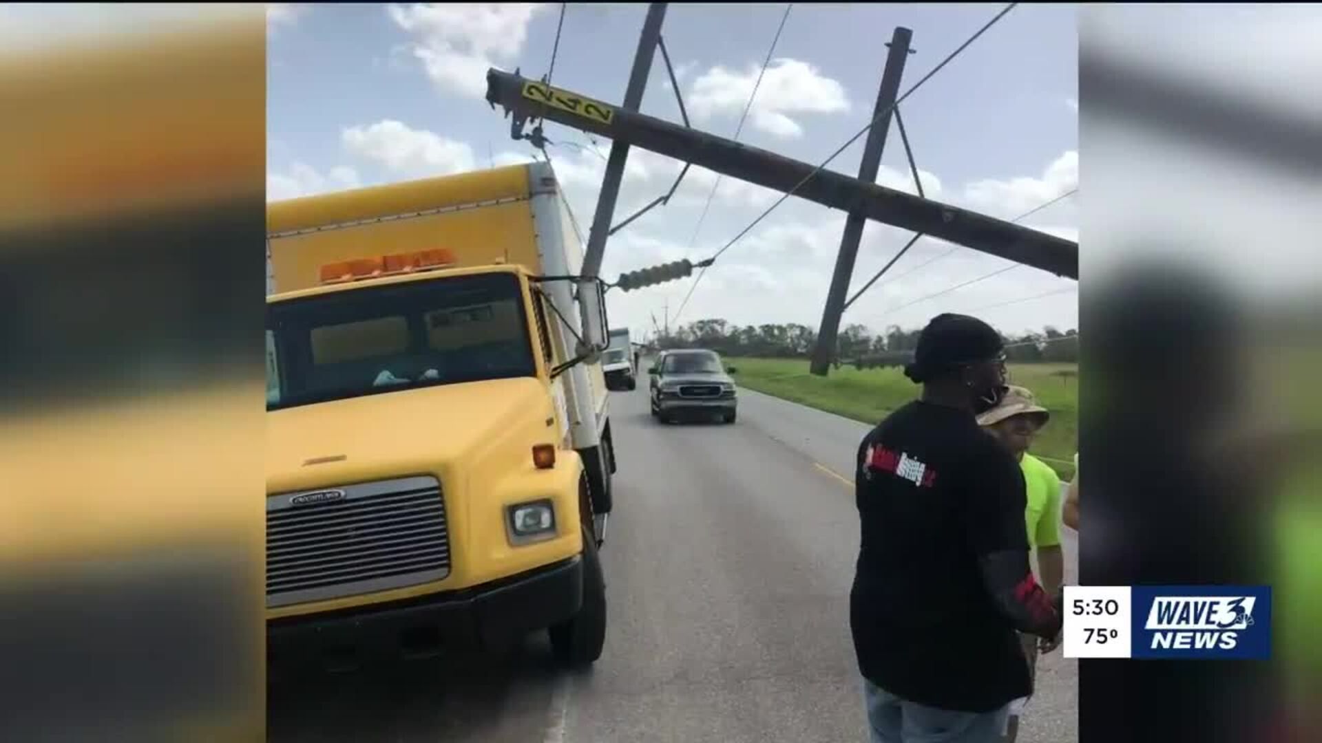 A utility pole lies across a road, near a yellow truck and two people.