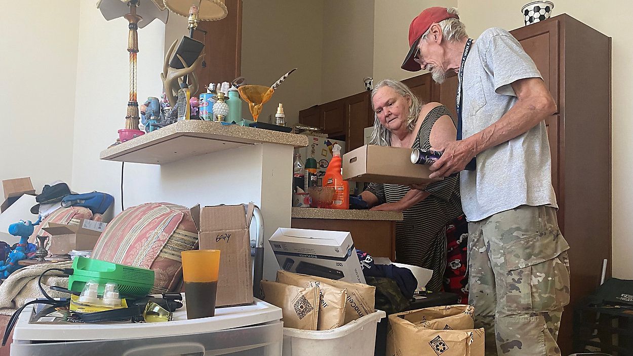 A cluttered room with a man and woman sorting through boxes.