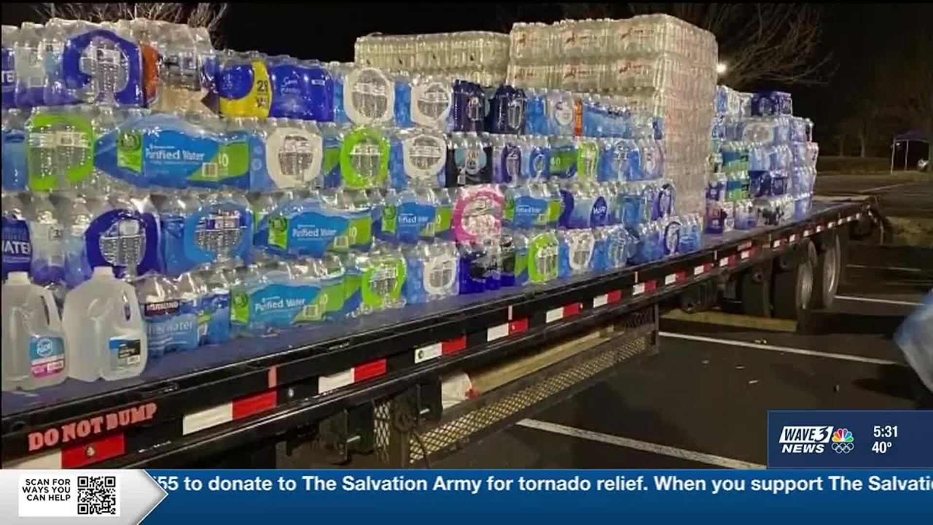 Flatbed truck loaded with bottled water for tornado relief, in a dark parking lot. Text on bottom.