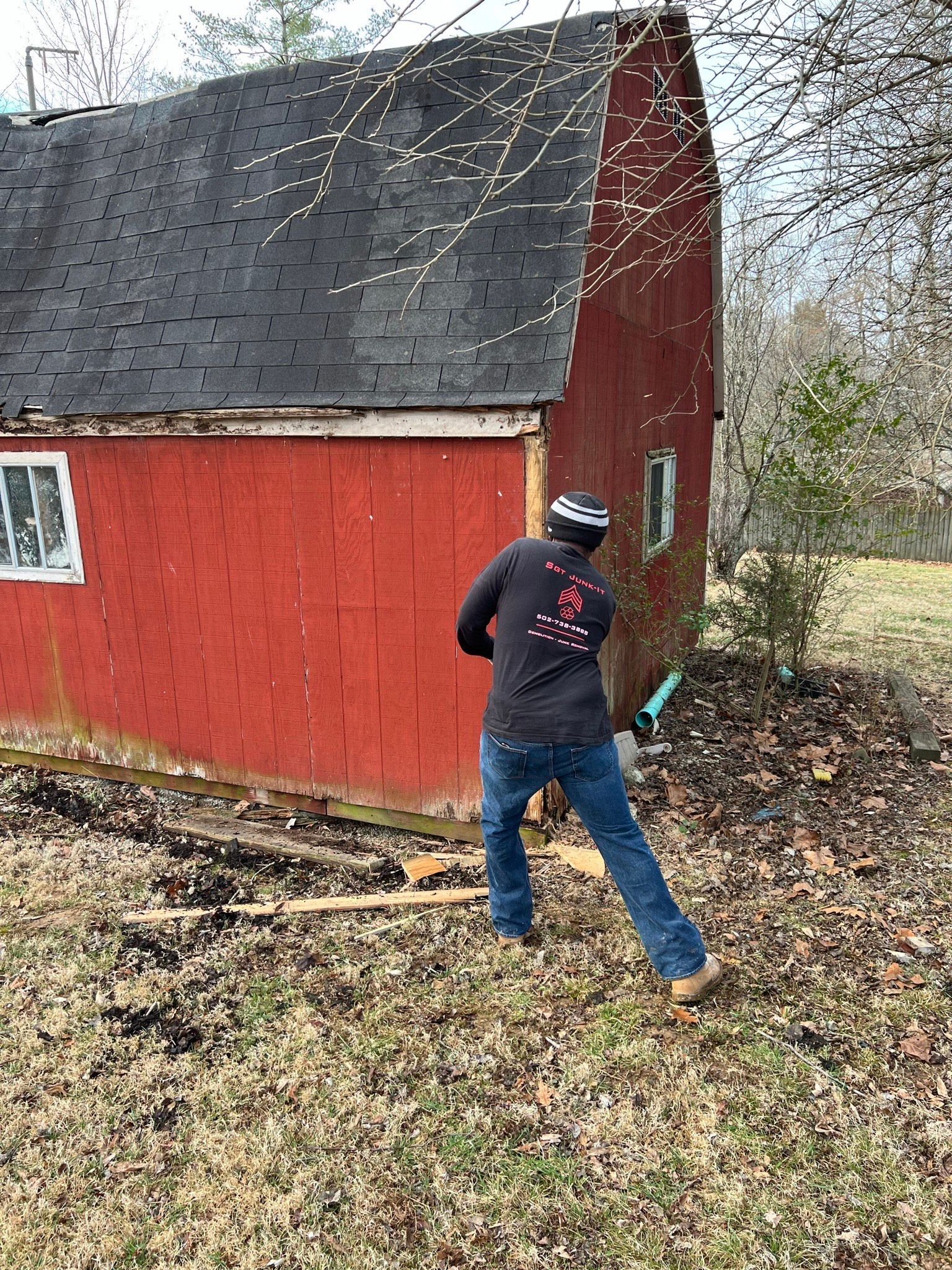 Person using a saw to demolish a red wooden shed.