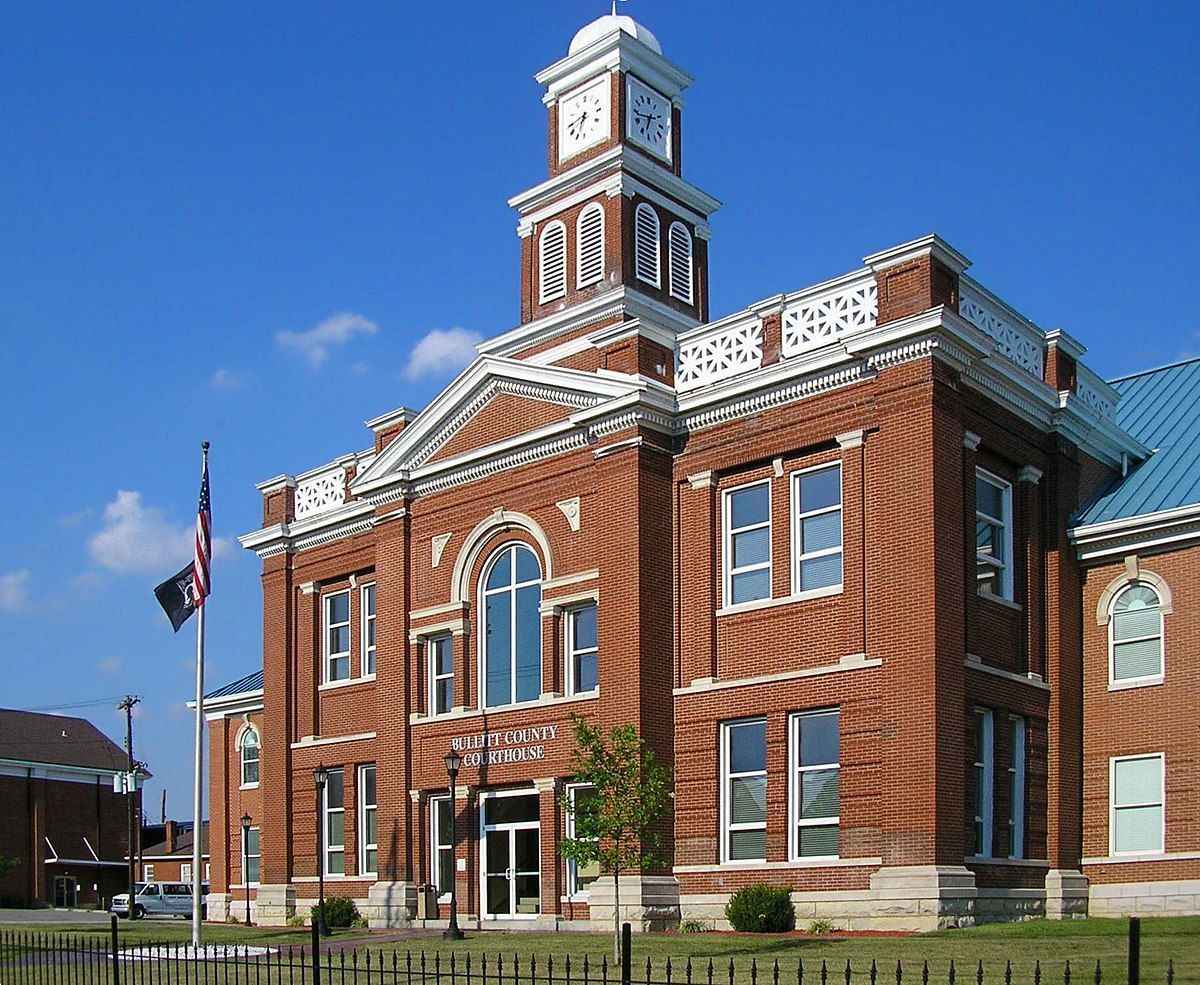 Brick courthouse with a clock tower against a blue sky; flag in front.
