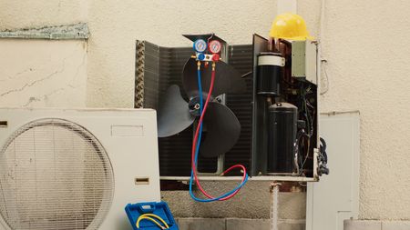 AC unit being serviced. Technician's gauges attached; unit's parts exposed. Fan and condenser visible.