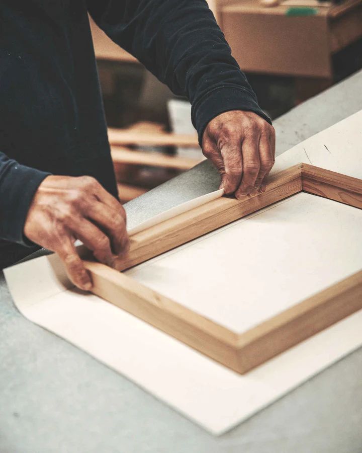 A person is holding a wooden frame on a table.