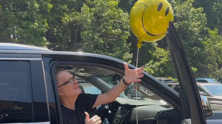 A man is sitting in a car holding a smiley face balloon.