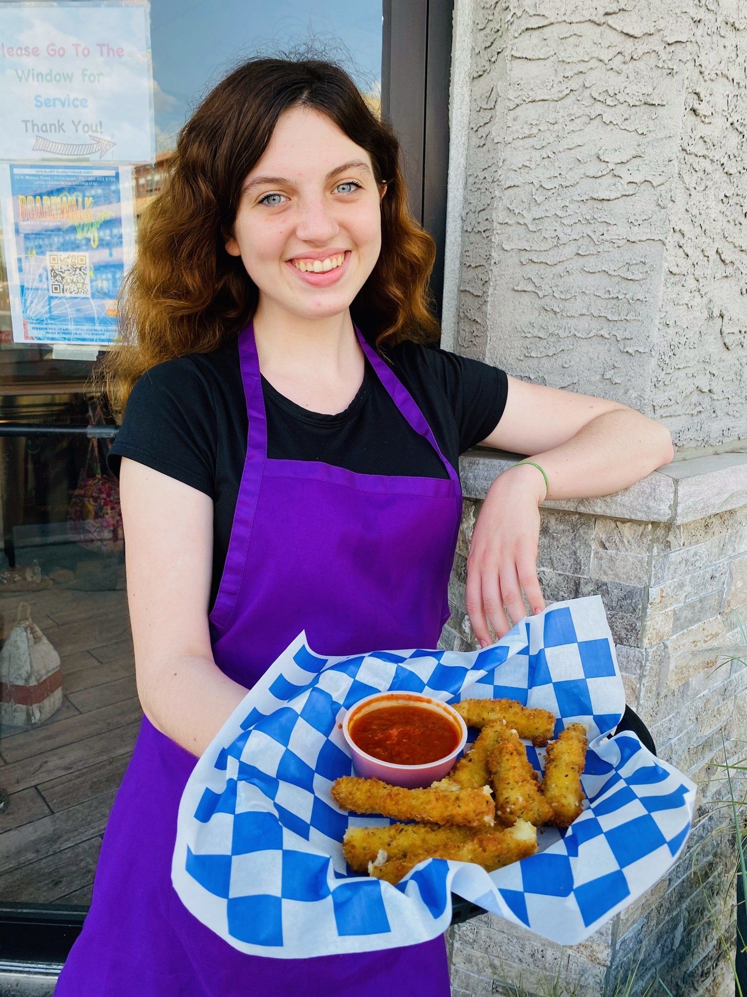 A woman in a purple apron is holding a plate of food.