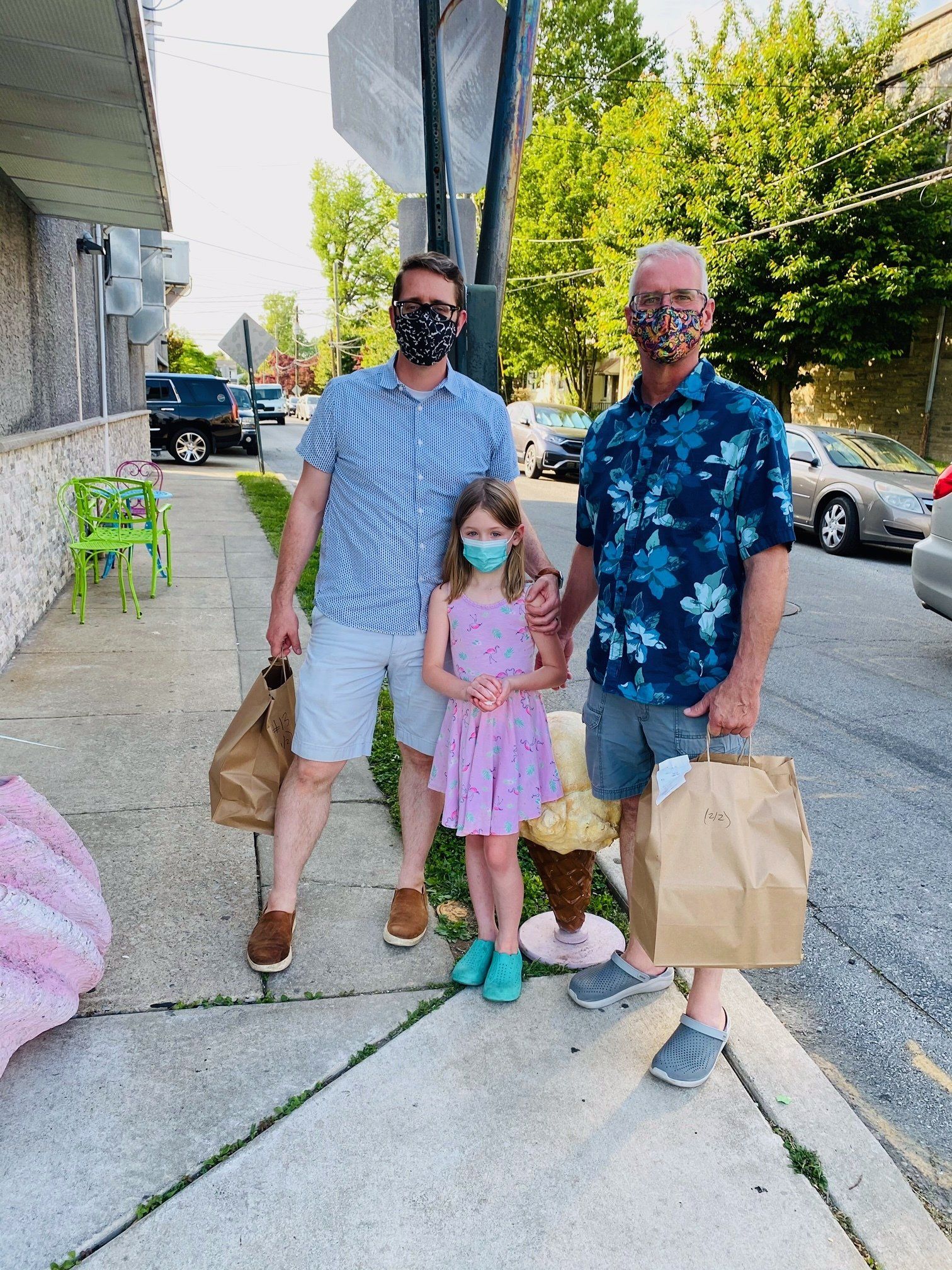 Two men and a little girl wearing face masks are standing on a sidewalk.