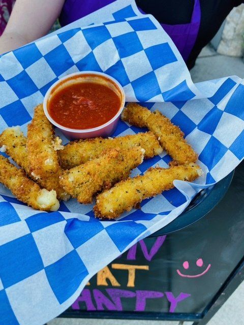 A person is holding a basket of cheese sticks with a dipping sauce
