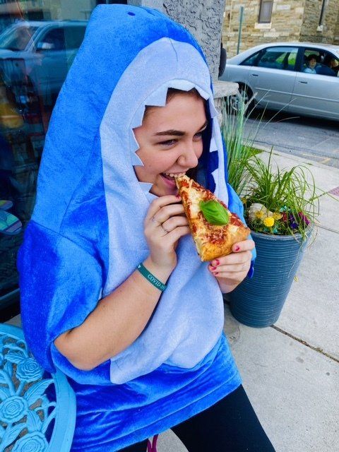 A woman in a shark costume is eating a slice of pizza