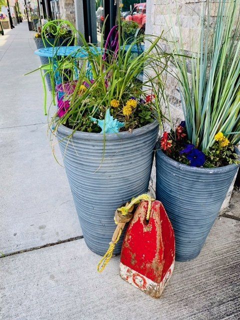 A red buoy is sitting on the sidewalk next to two potted plants.