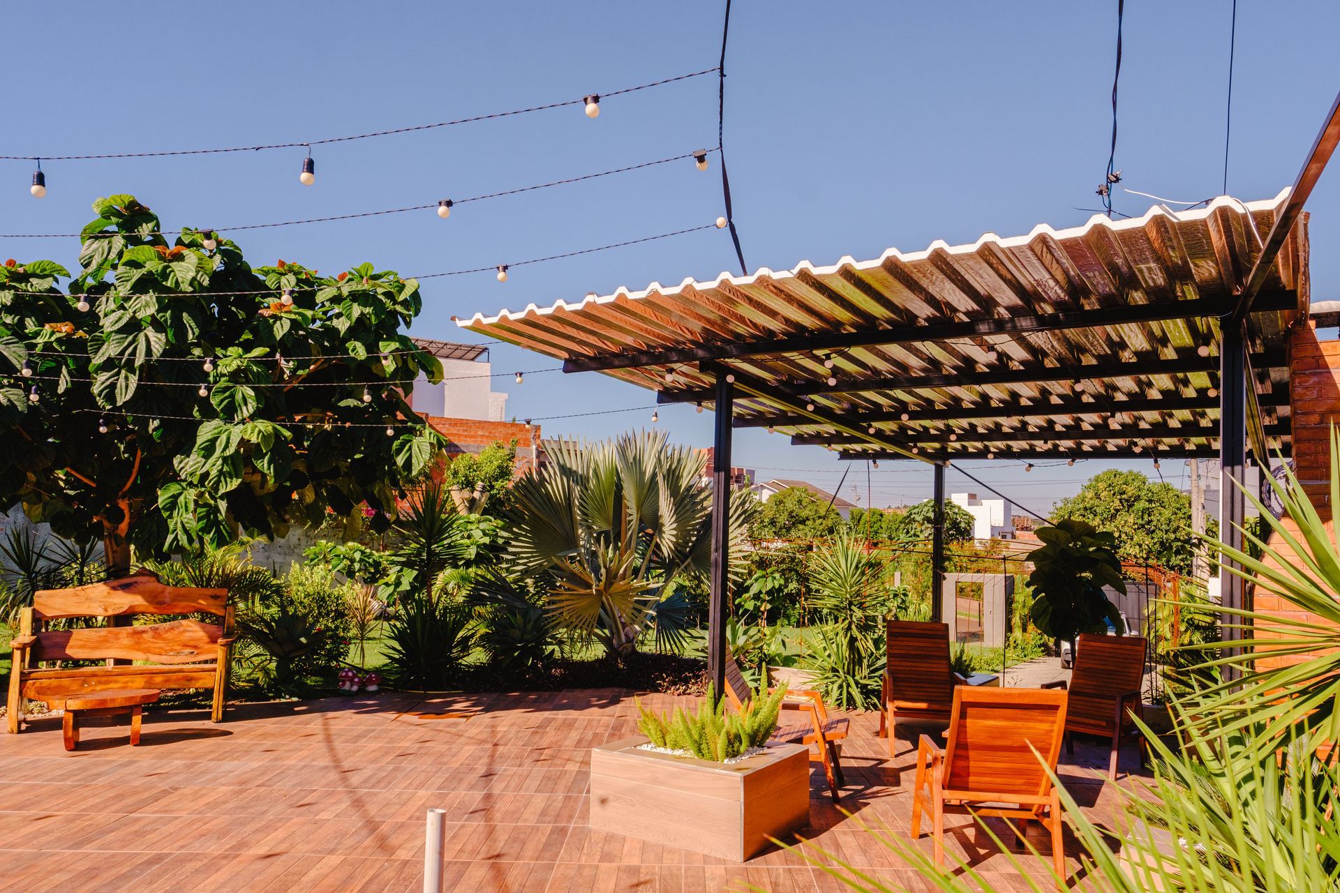 Pátio externo com móveis de madeira, luzes de corda e telhado de zinco.