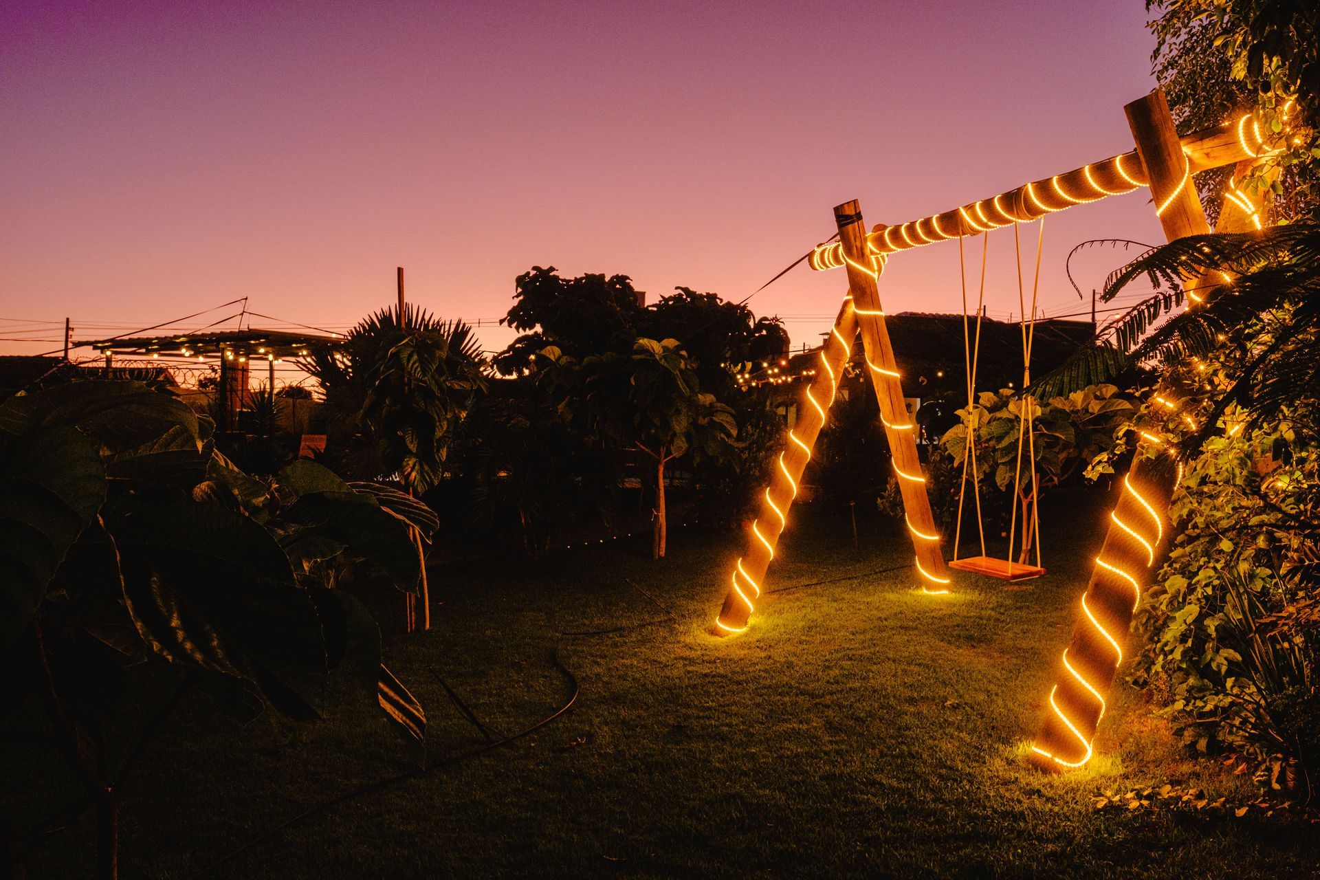Um balanço de madeira envolto em luzes aconchegantes, tendo como pano de fundo um céu crepuscular em um jardim.