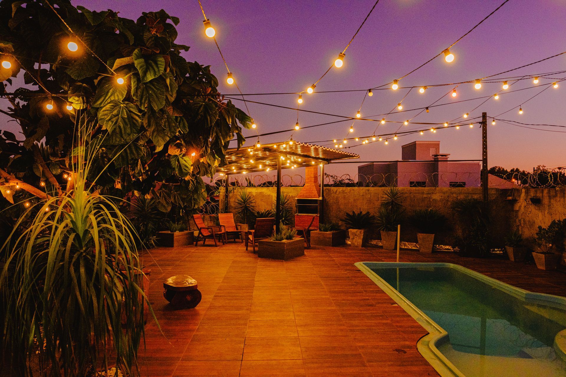 Pátio externo ao entardecer com luzes de corda, piscina pequena e áreas de estar.