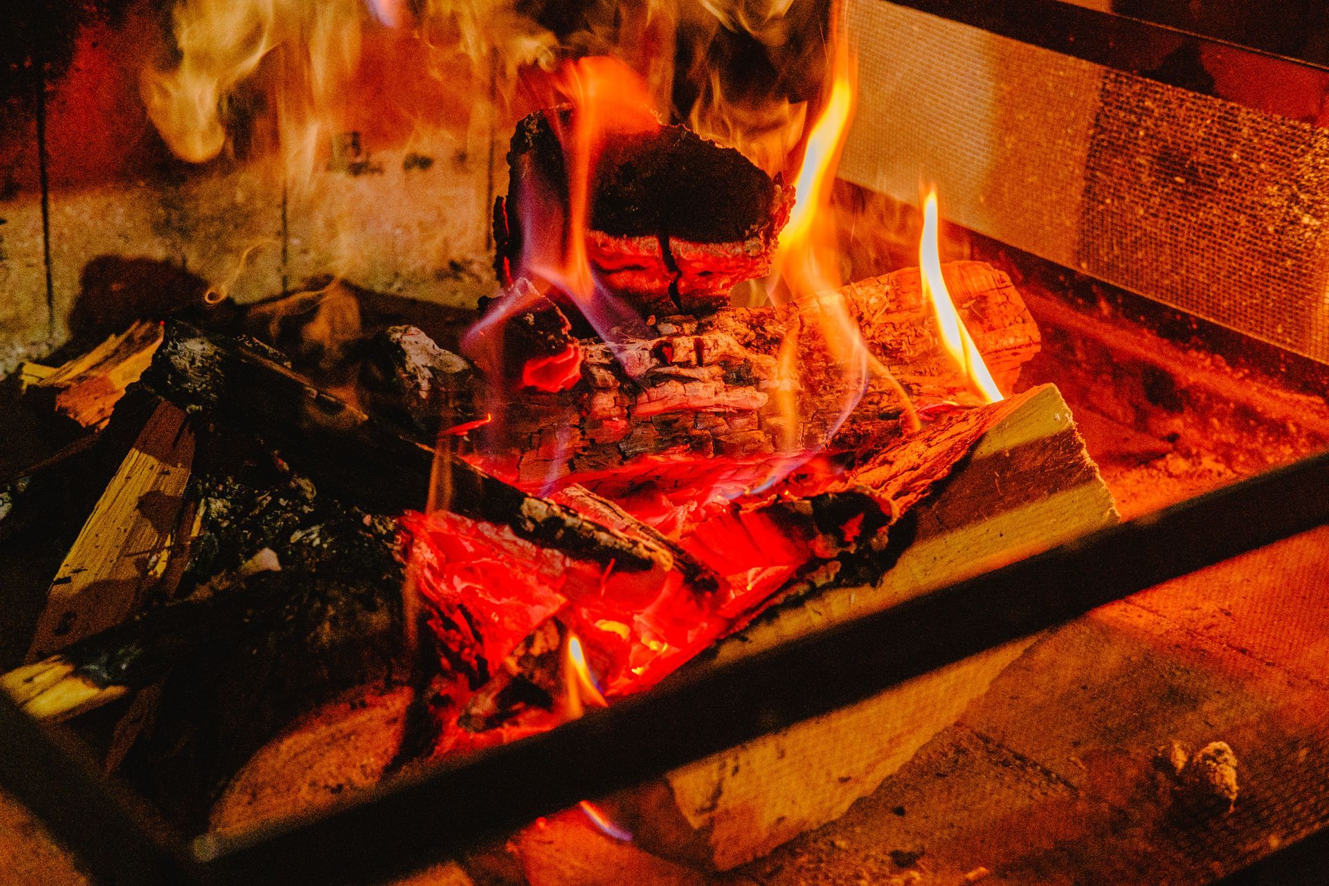 Fogo aceso dentro de uma lareira de tijolos, com chamas e brasas vermelhas incandescentes.
