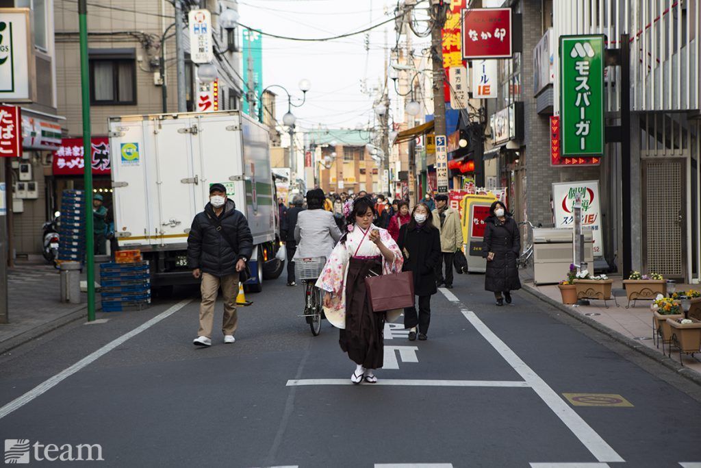 This street in Japan shows how Japanese culture looks very different from American culture. The people are dressed differently, signs are in Japanese, and there are many colorful signs.