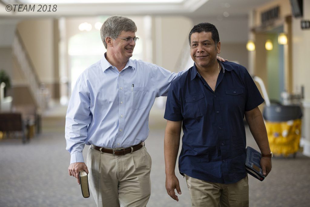 An American missionary and a Hispanic member of the church walk together carrying Bibles.