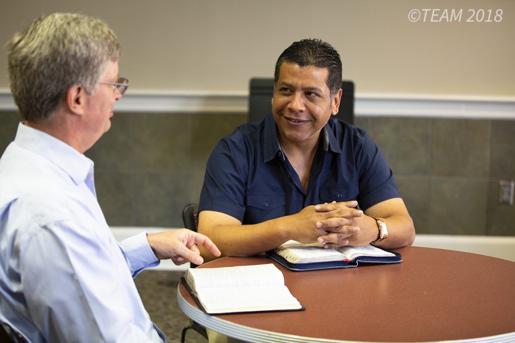 Julio and Keith Moore sit at a table and study the Bible together.
