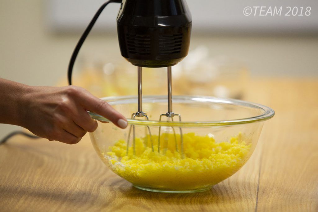 The baker uses a hand mixer to combine the ingredients.