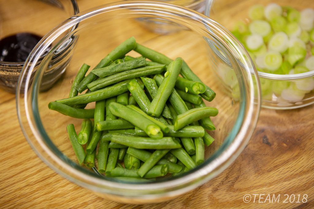 The green beans are cut diagonally and place in a glass bowl.