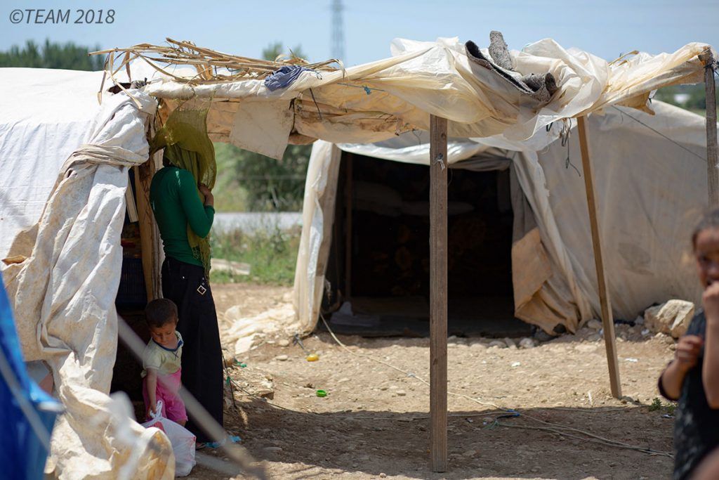 A refugee mother and her child stand underneath a tent at the refugee camp