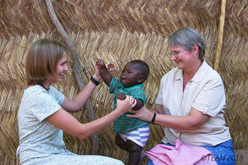 A missionary and her daughter in Africa play with a small child,