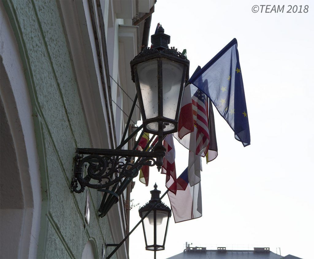 A lamp post in France has several different countries' flags hanging by it.