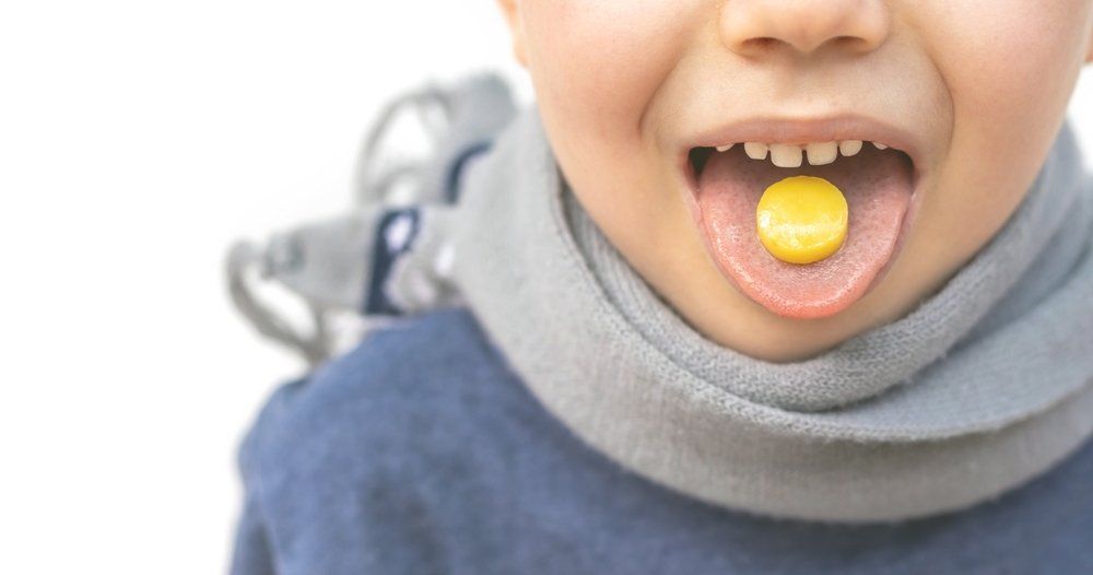 a boy with a throat lozenge in his mouth made with sugar to make it taste good for kids