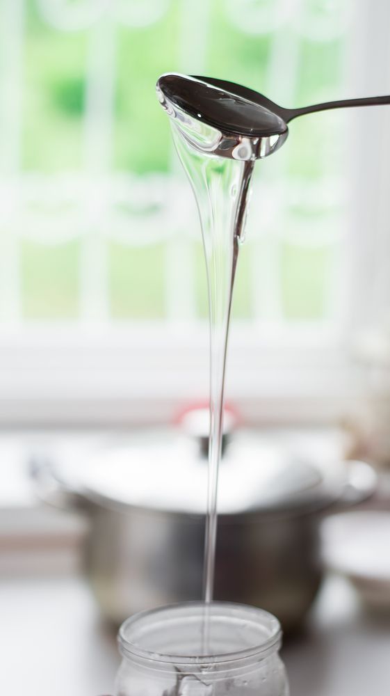 Corn syrup being poured from a spoon into a jar.