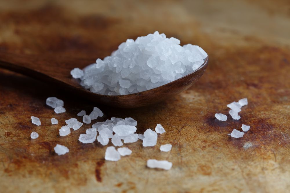 A wooden spoon filled with sea salt on a table.